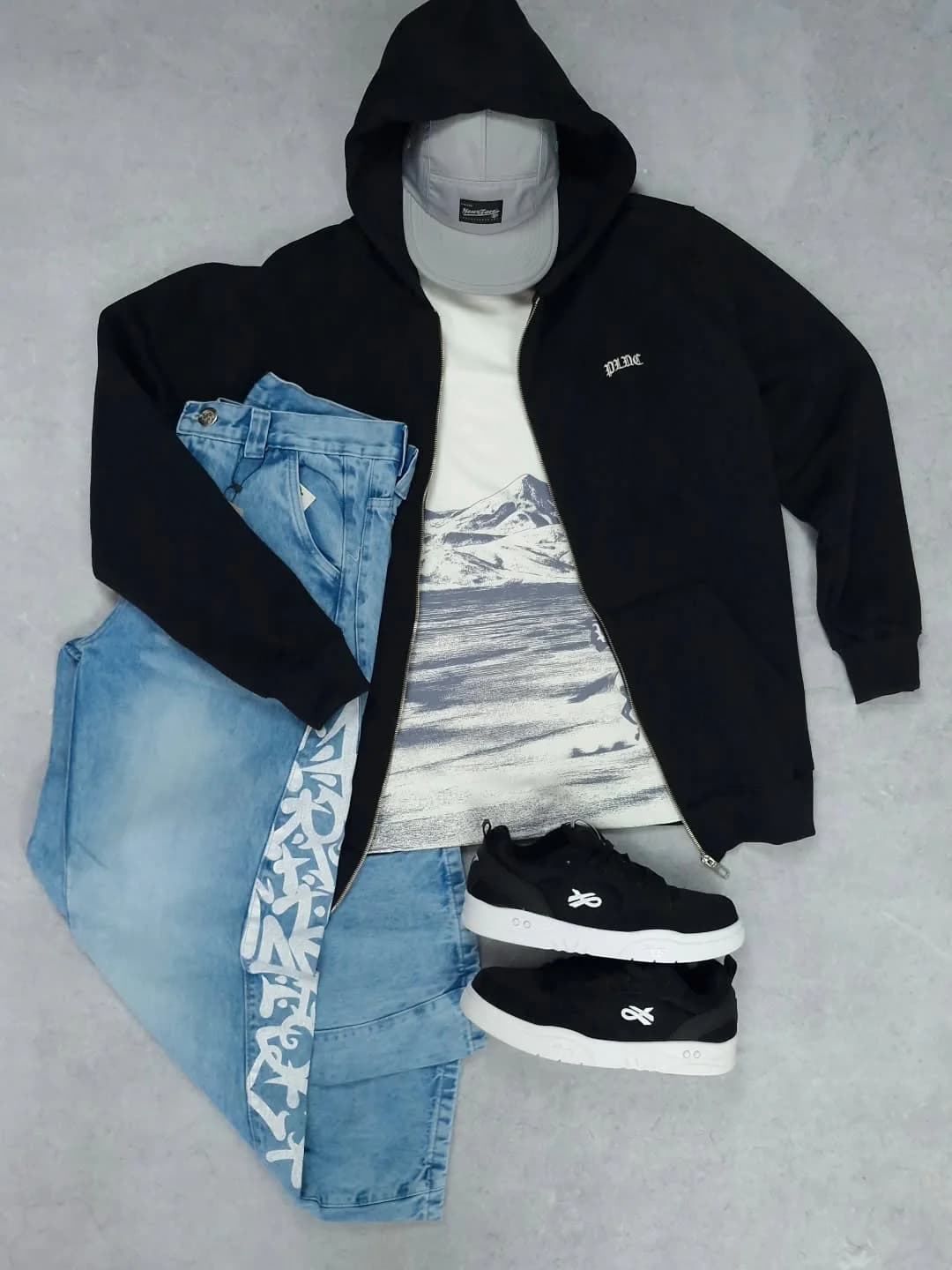 Kit no concreto: moletom com zíper preto, camiseta com a montanha, calça clara com recorte e tênis ÖUS preto