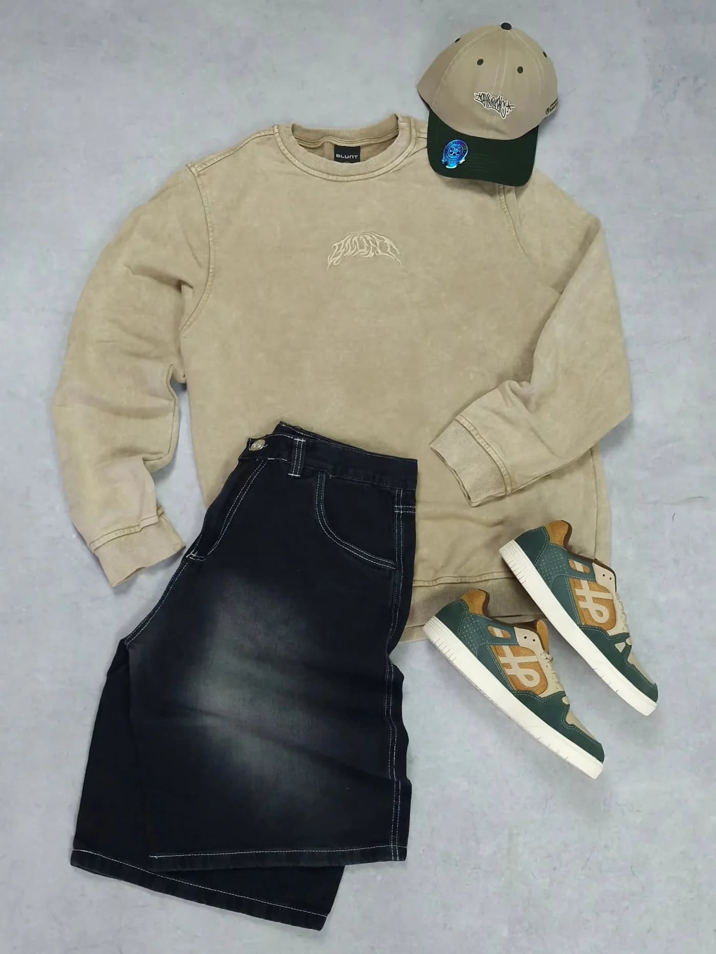 Kit no concreto: moletom bege, bermuda jeans preta, boné verde e tênis ÖUS verde