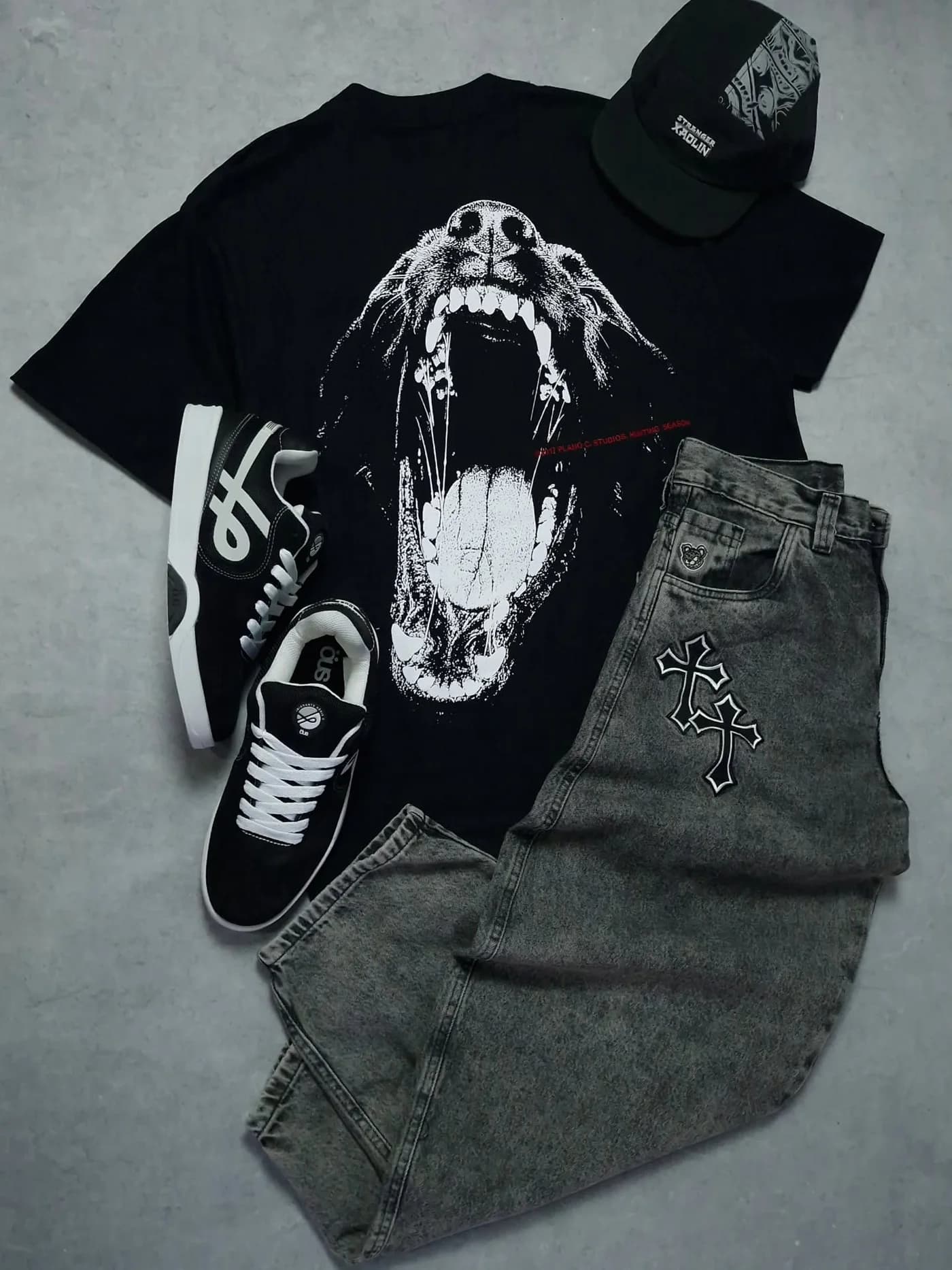 O kitzão de 31 de agosto no chão de concreto: camiseta Plano C com o cachorro, calça jeans cinza, boné Stranger x Xaolin e tênis ÖUS